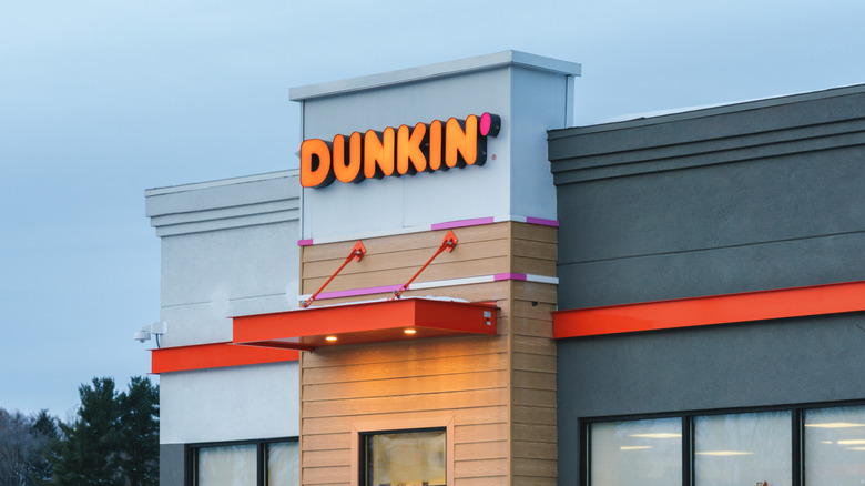 The exterior of a Dunkin' restaurant, seen at dusk or dawn, with the logo illuminated
