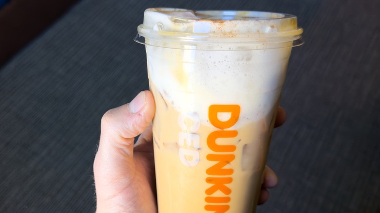A hand holds a Dunkin' iced coffee with cold foam on top