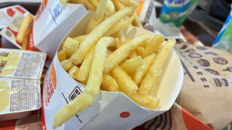 A cup of Burger King fries, next to sauce packets and burger wrappers