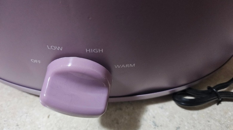 A close-up of a purple Crockpot with a dent in the housing