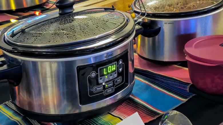 A Crockpot set to "low" on a colorful tablecloth next to another Crock-Pot filled with chili