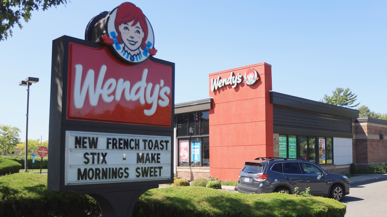A Wendy's restaurant has a car going through the drive-thru.
