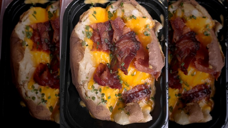 A Wendy's baked potato is topped with bacon in a takeout container.