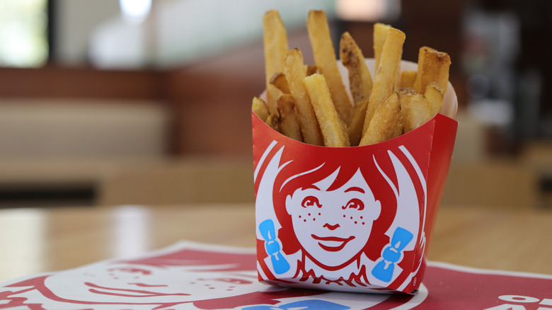 Wendy's fries are in a carton on a table in the restaurant.