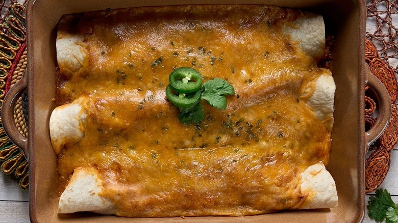Cooked chicken enchiladas in a pan topped with cheese and jalapeño slices