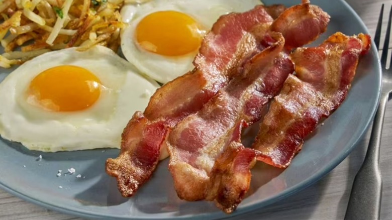 Two eggs, hash browns, and cooked bacon on a blue plate