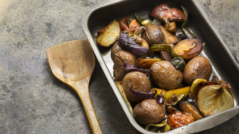 A pan full of roasted potatoes and veggies on a table with a wooden spoon
