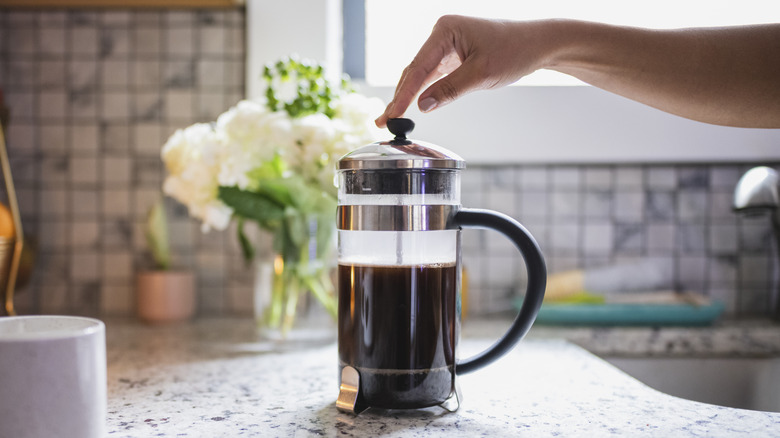 A hand pushing down French press on countertop