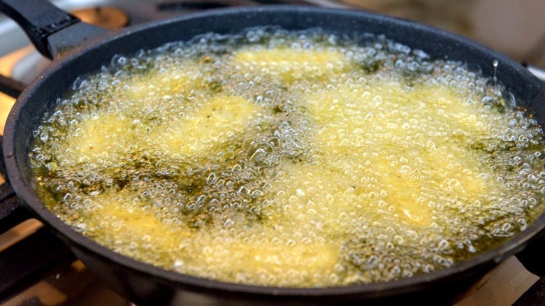 Food frying underneath a lot of hot, bubbling oil in a pan