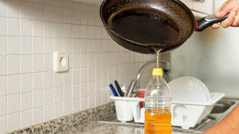 A hand pouring used oil from a frying pan back into the bottle