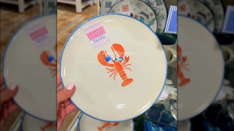 A hand holds a plate with a Made In Portugal sticker and lobster art