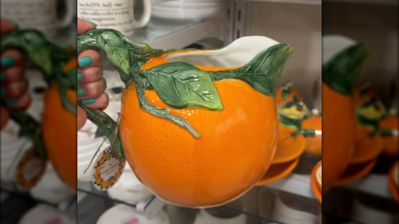 A hand holds up an orange-shaped pitcher at a HomeGoods store.