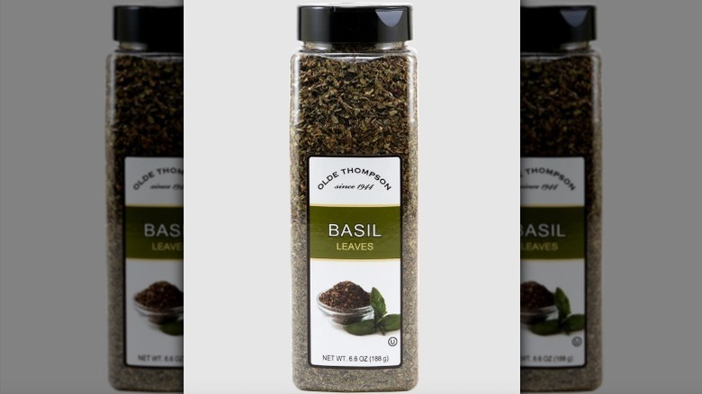 Container of dried basil on white background