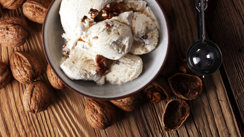 Overhead view of a bowl of walnut ice cream, walnut shells, and a vintage scoop on a wooden surface