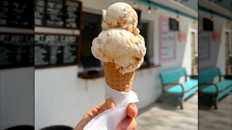 A hand holding up a double scoop cone of butter brickle ice cream