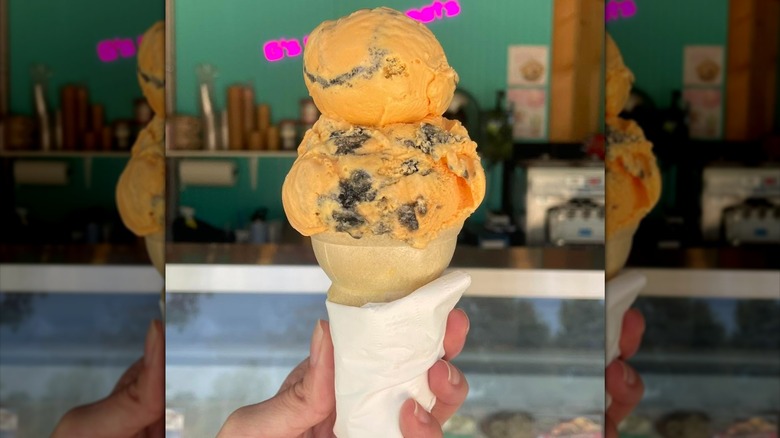A hand holding up a double scoop cone of tiger tail ice cream