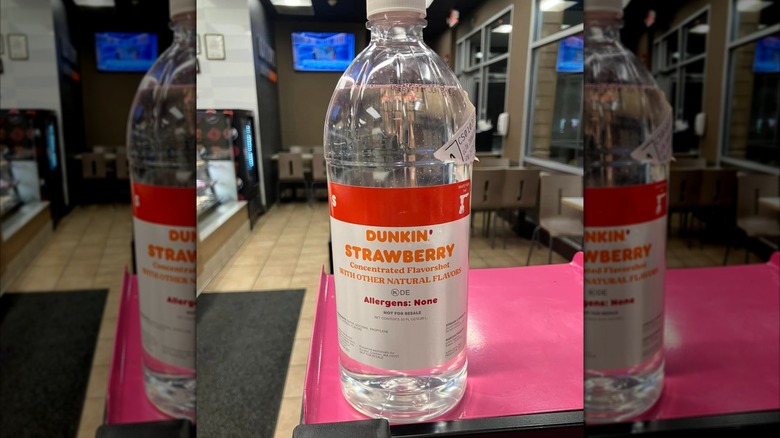 A bottle of Dunkin' Strawberry Concentrated Flavorshot, displayed in a Dunkin' restaurant