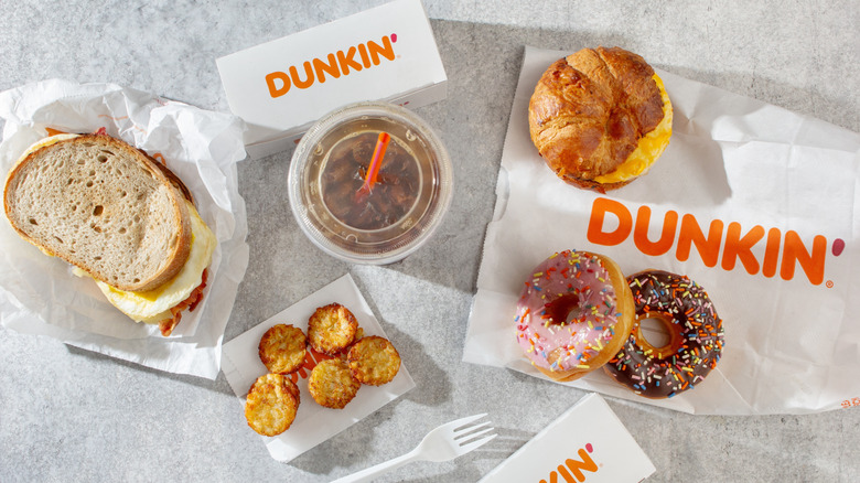 A variety of Dunkin' breakfast items -- including coffee, sandwiches, and donuts -- arranged on a table
