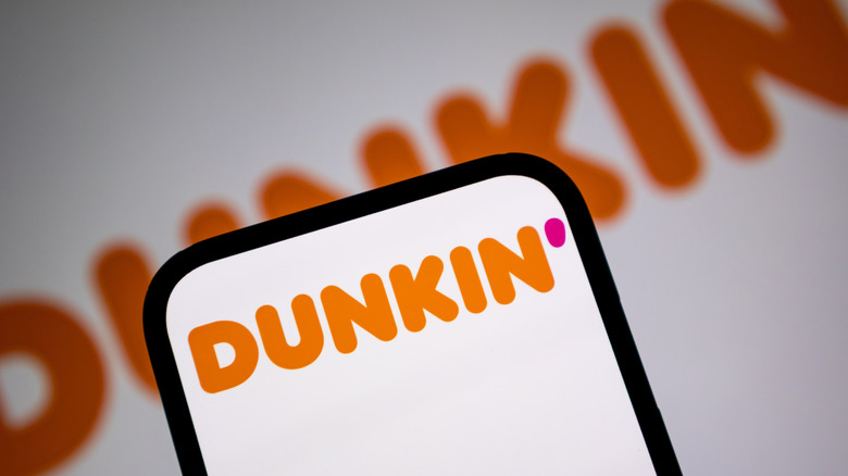 The Dunkin' logo is prominently displayed on a smartphone, with the logo out of focus in the background