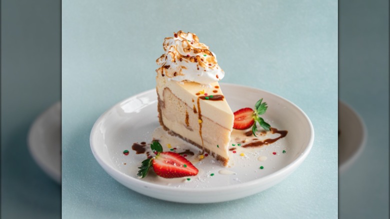 A slice of tres leches cake with meringue and strawberries on a white plate against a blue background