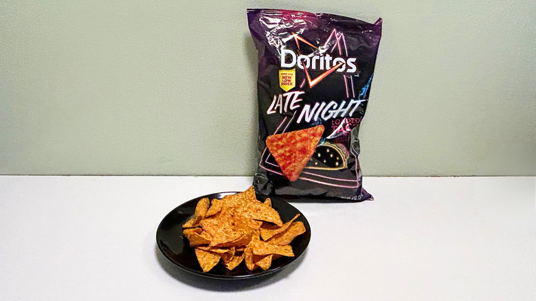 A bag of Doritos Late Night Loaded Taco next to a black plate of chips
