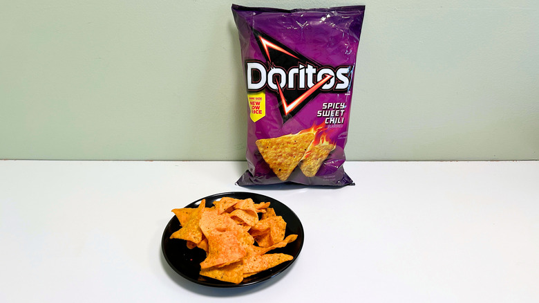 A bag of Doritos Spicy Sweet Chili next to a black plate of chips