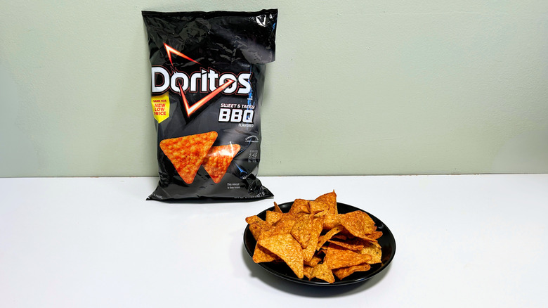 A bag of Doritos Sweet and Tangy BBQ next to a black plate of chips