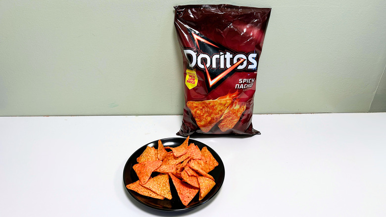 A bag of Doritos Spicy Nacho next to a black plate of chips