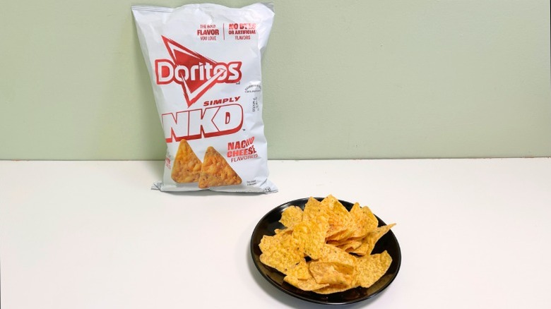 A bag of Doritos Simply NKD Nacho Cheese next to a black plate of chips