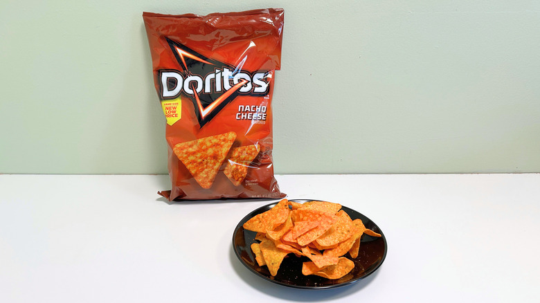 A bag of Doritos Nacho Cheese next to a black plate of chips