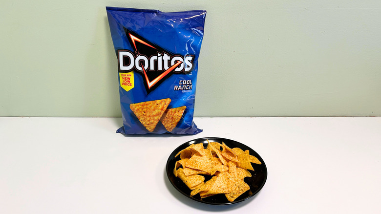 A bag of Doritos Cool Ranch next to a black plate of chips