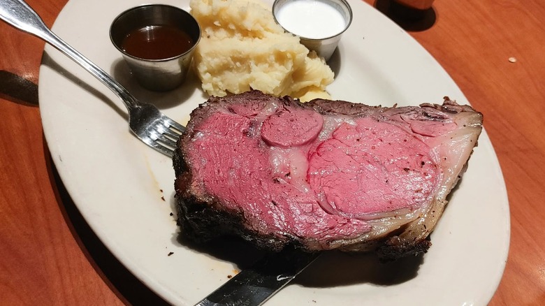 A Black Angus Steakhouse prime rib dinner with ramekins of sauce and mashed potatoes