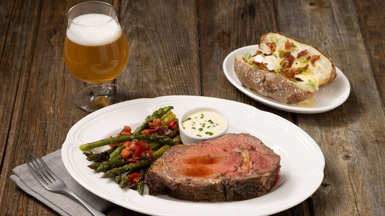 J. Gilbert's Steakhouse prime rib meal with asparagus on a white plate and a potato and beer on the side