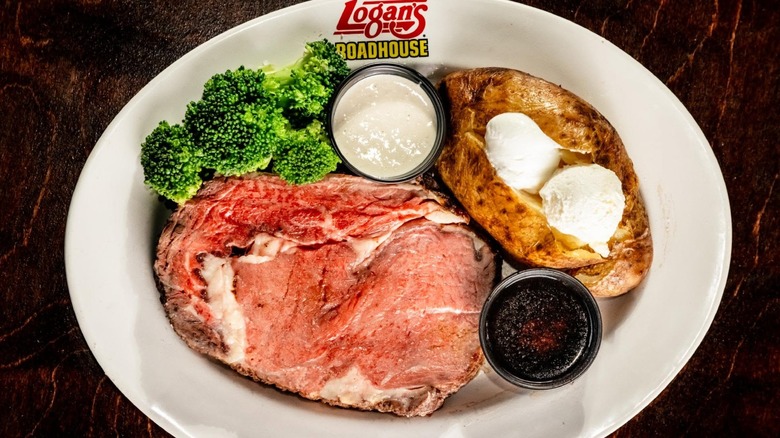 Prime rib with broccoli, horseradish sauce, and a baked potato on a Logan's Roadhouse-branded white plate
