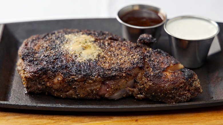 A Perry's Steakhouse carmelized prime rib on a black plate with ramekins of sauce