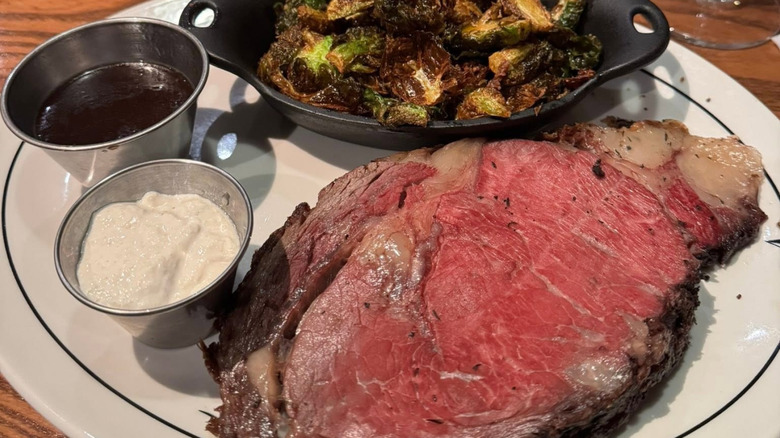 Saltgrass Steakhouse's prime rib with Brussels sprouts and ramekins of sauce on a white plate