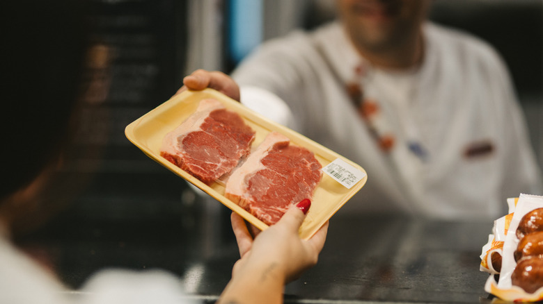 A butcher handing a customer a package of steaks at a grocery store