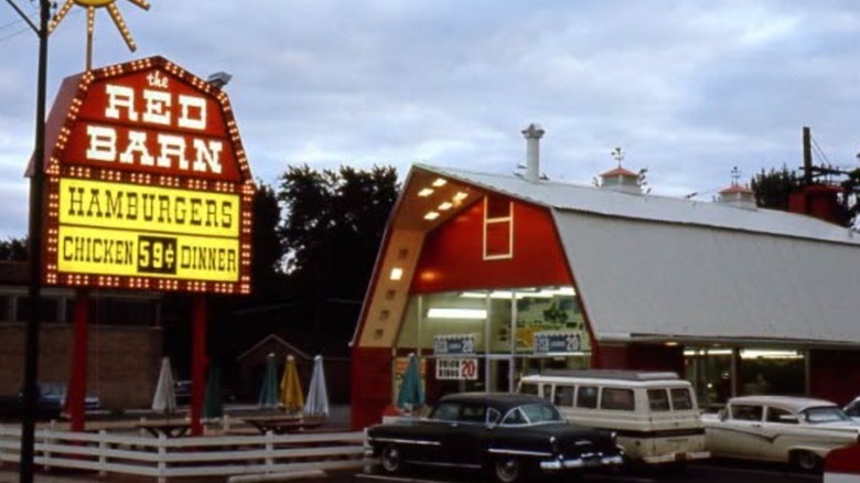 A vintage image of a Red Barn restaurant, with a road sign on the outside and several cars parked in its parking lot