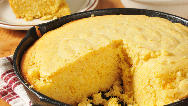 A cast iron with cornbread and a slice taken out