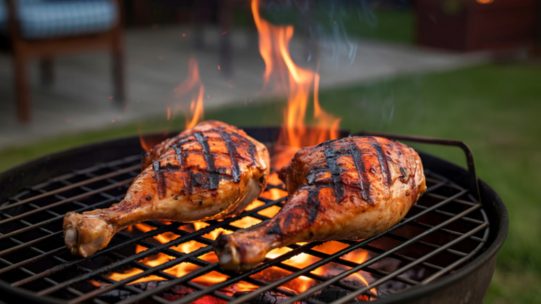 Two chicken drumsticks grilling over a fire outside