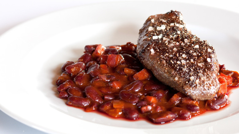 A white plate with baked beans and a cooked steak