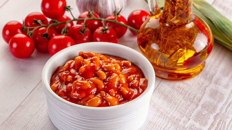 A ramekin of baked beans with cherry tomatoes on the vine behind it