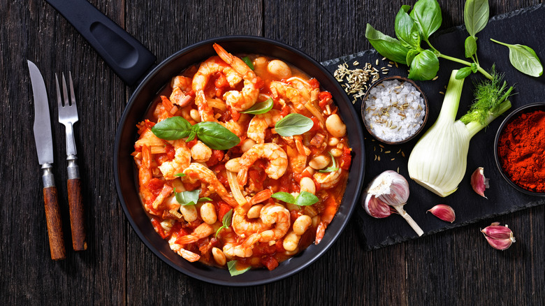 A pan with shrimp and beans garnished with basil