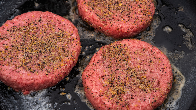 Seasoned burger patties cooking