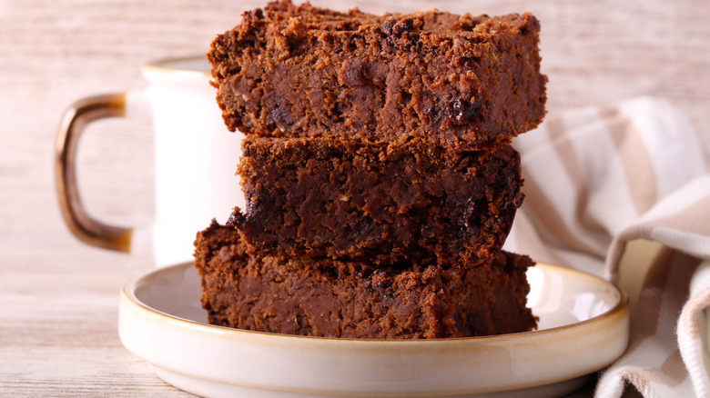Three brownies stacked on top of each other on a plate, placed on a wooden table