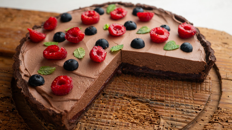 Chocolate pie topped with fresh raspberries, blueberries, and mint leaves on a wooden table