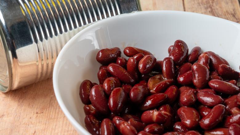 Canned kidney beans in a white bowl and an empty can on a wooden table