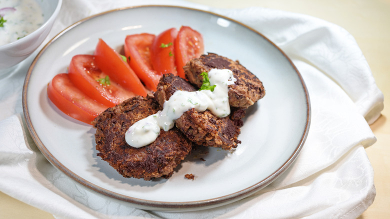 Kidney bean kebabs topped with yogurt and served with sliced tomatoes on a white plate