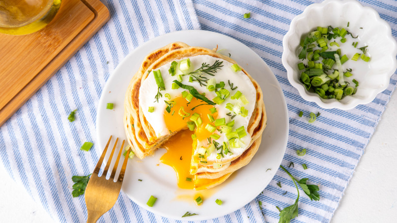 Pancakes topped with a sunny side up and chopped scallions on a white plate