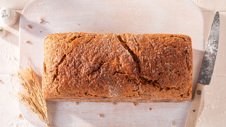 A whole loaf of bread on a wooden chopping board with a knife